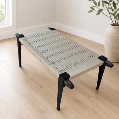 A woven bench with black metal legs sits on a wooden floor in a room with a window.