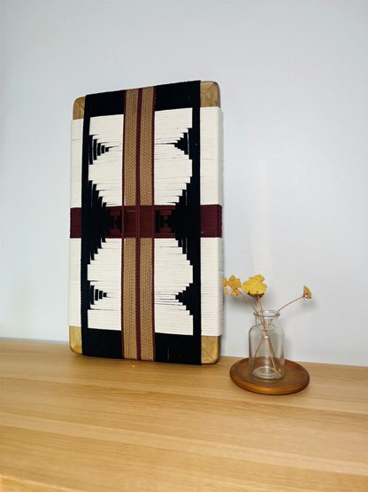 a wooden shelf with a decorative woven piece and a small vase with yellow flowers placed on it.