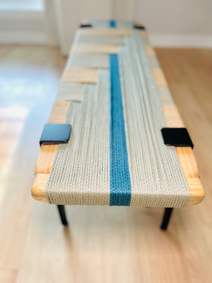 a wooden bench with a woven seat and a blue stripe running down the center. The bench has black metal clamps on the sides.