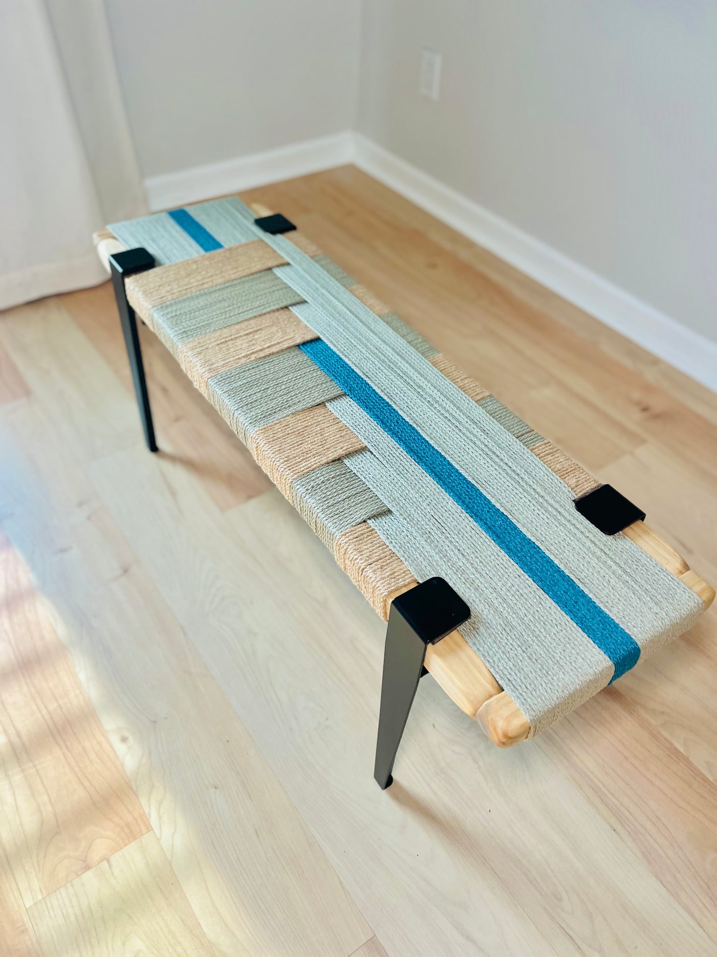 a wooden bench with a woven seat and legs, placed on a wooden floor.