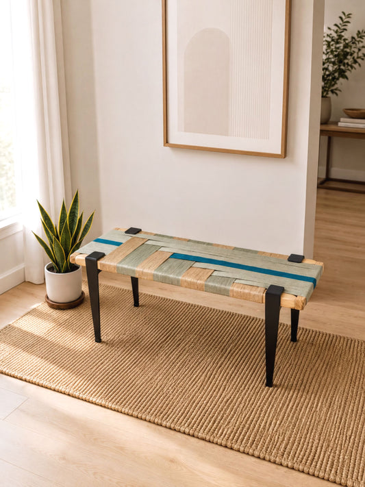 a wooden bench with a woven seat and legs, placed on a woven rug in a room with a window and a plant.