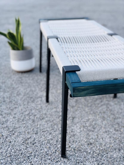 a white bench with a blue frame, placed on a gravel surface next to a potted plant.