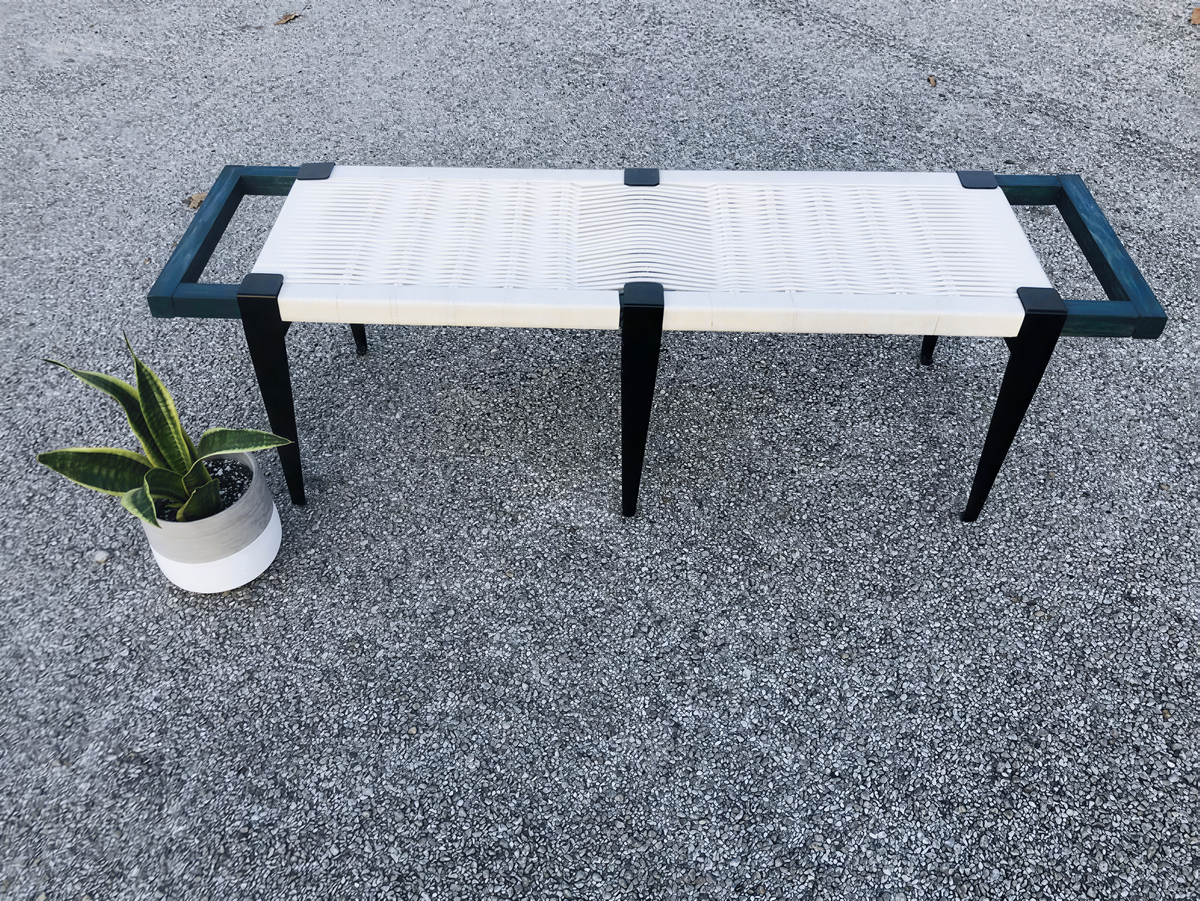 a bench with a white seat and black metal legs, placed on a gray surface. Next to the bench is a potted plant, adding a touch of greenery to the scene.