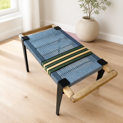 A blue woven bench with a wooden frame sits on a wooden floor, accompanied by a white vase with a plant on the side.