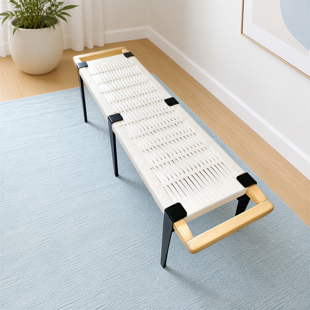 a modern, minimalist bench with a woven seat and wooden frame, placed on a blue rug in a room with a white wall and a plant in a white pot.