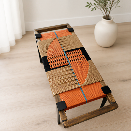 a wooden bench with an orange and black woven seat, placed on a wooden floor next to a white vase with a plant.