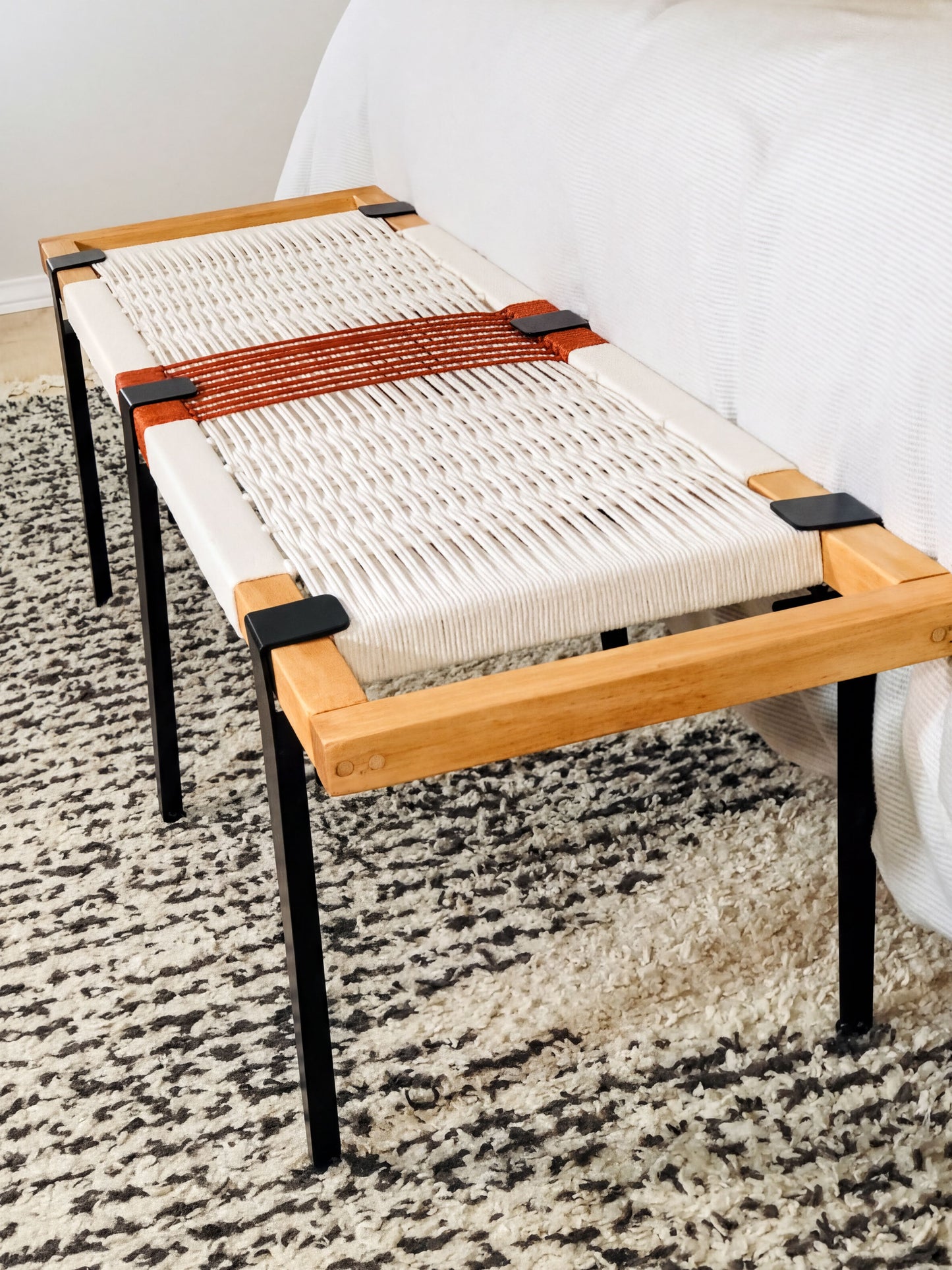 a modern bench with a woven seat and wooden frame, placed on a patterned rug.
