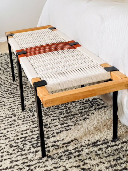 a modern bench with a woven seat and wooden frame, placed on a patterned rug.
