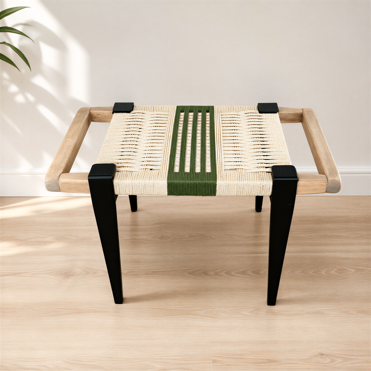 A modern, minimalist stool with a woven seat and black metal legs, placed on a wooden floor against a white wall.