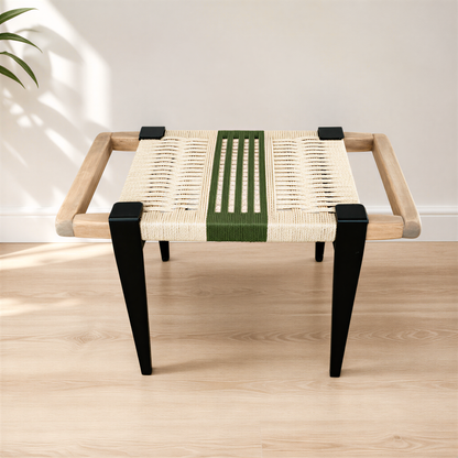 A modern, minimalist stool with a woven seat and black metal legs, placed on a wooden floor against a white wall.