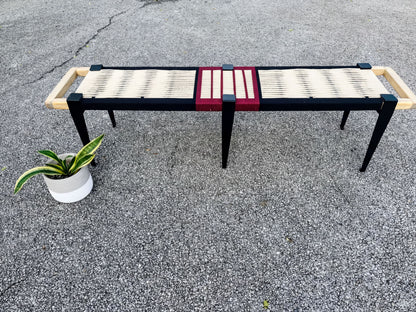 a bench with a black and red design, placed on a gray surface. Next to the bench is a potted plant, adding a touch of greenery to the scene.