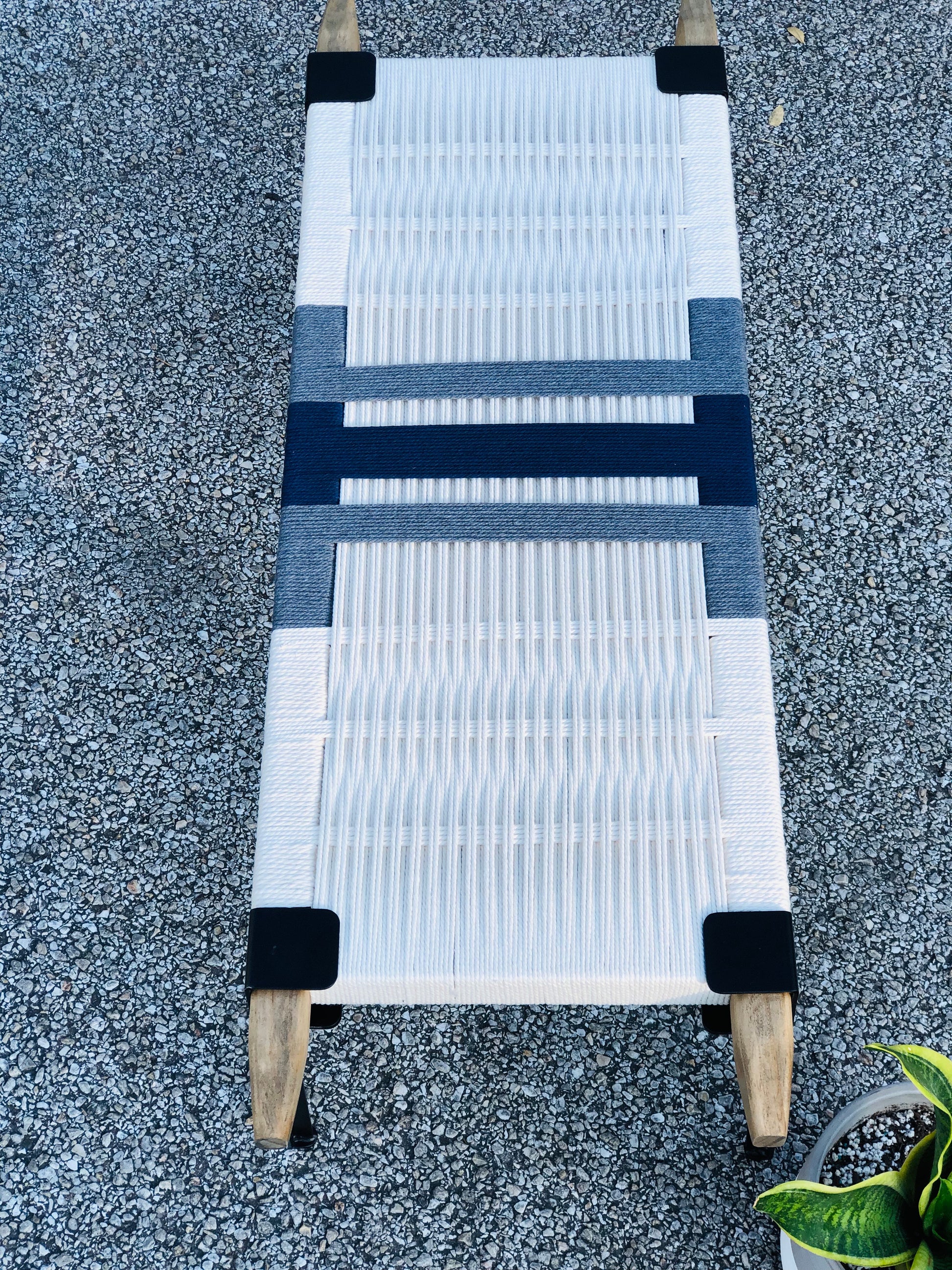 a white and blue woven bench or lounge chair placed on a gravel surface.