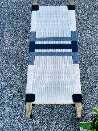 a white and blue woven bench or lounge chair placed on a gravel surface.